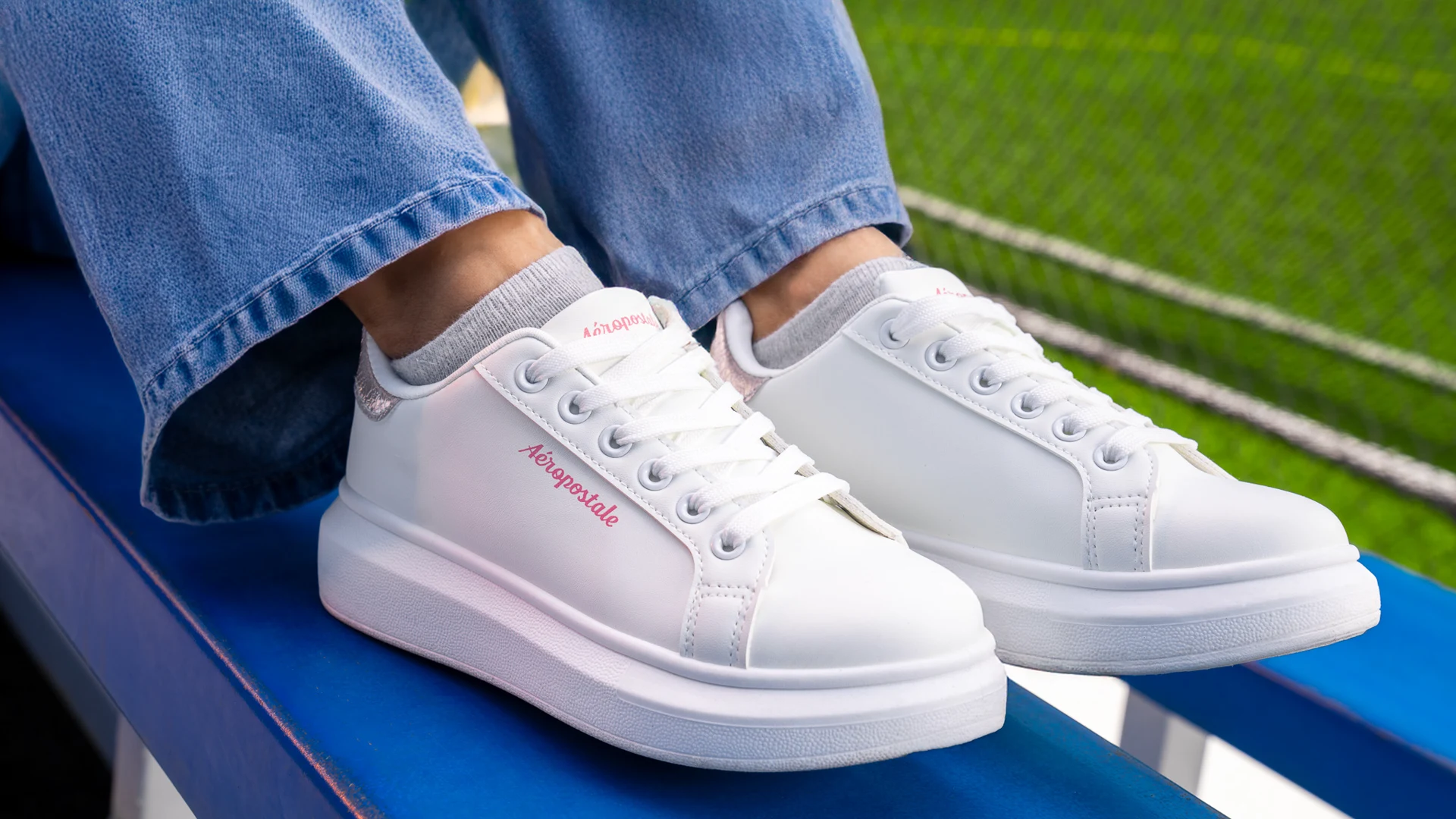 Detalle de producto de la campaña Aeropostale por ZerezoFilms: tenis blancos con logo rosa sobre una grada azul junto a la cancha